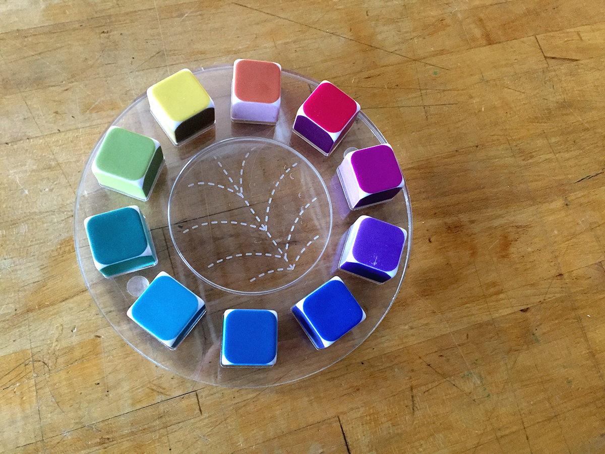 a color wheel, where each color is made of dice. Dice are on a clear plastic tray, with lines at the center to show color relationships like triads and split complementaries.