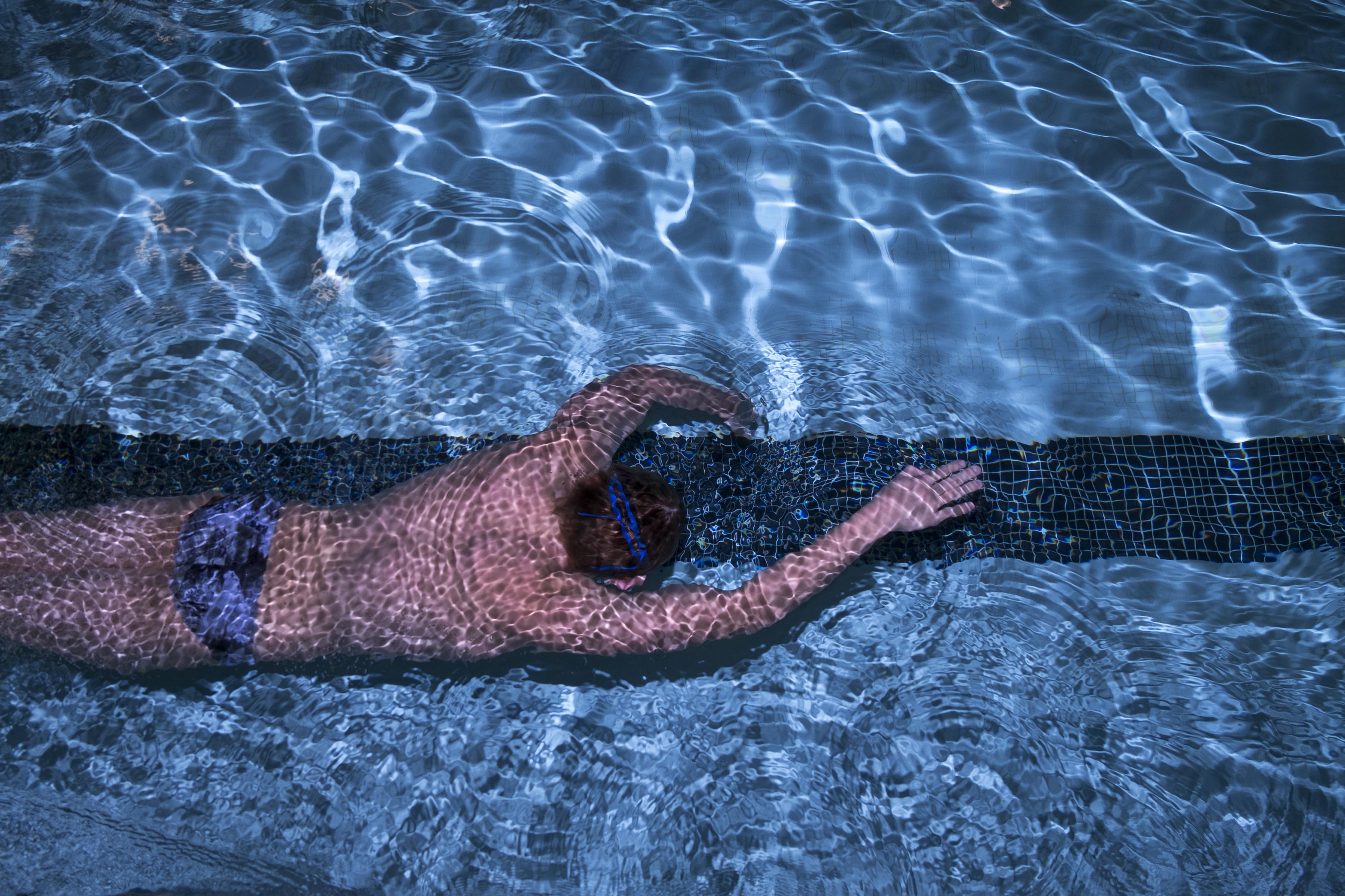 A photograph of a man in a speedo swimming in a pool, shot from above.